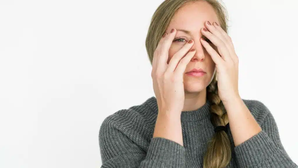A woman covers part of her face with her hands against a plain background.