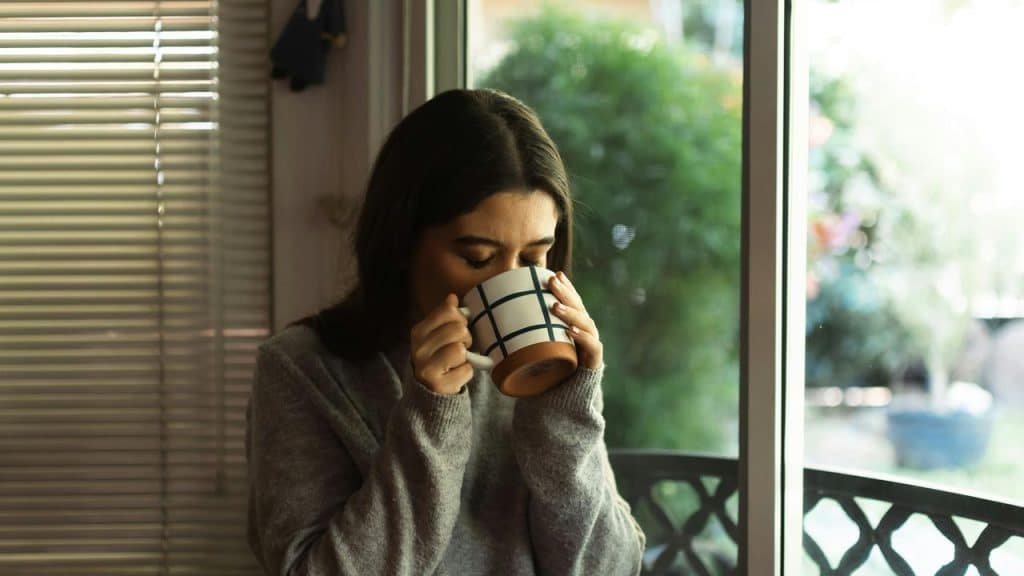 A woman in a cozy sweater sipping a mug by a sunlit window.