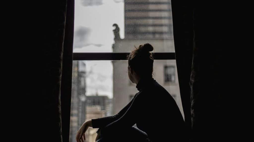 A person sitting in silhouette by a window, looking out at city buildings.