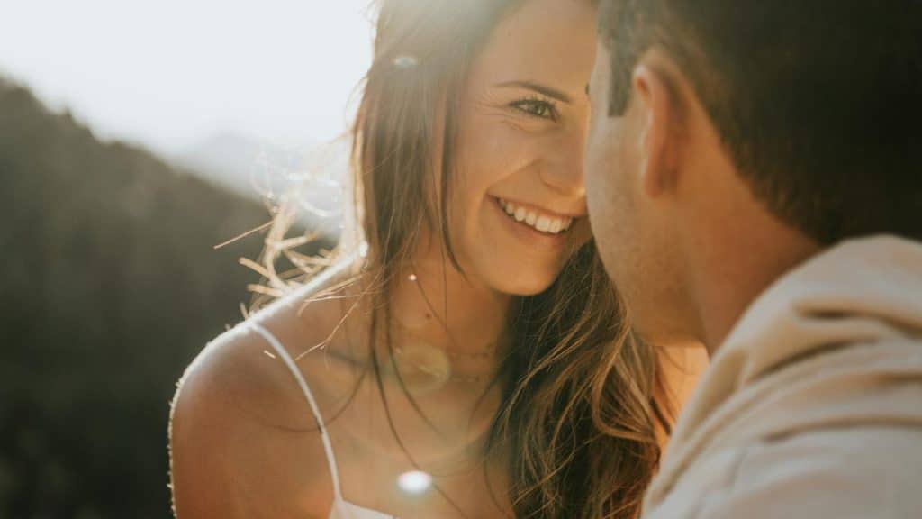 A smiling woman gazing closely at a partner in warm sunlight outdoors.