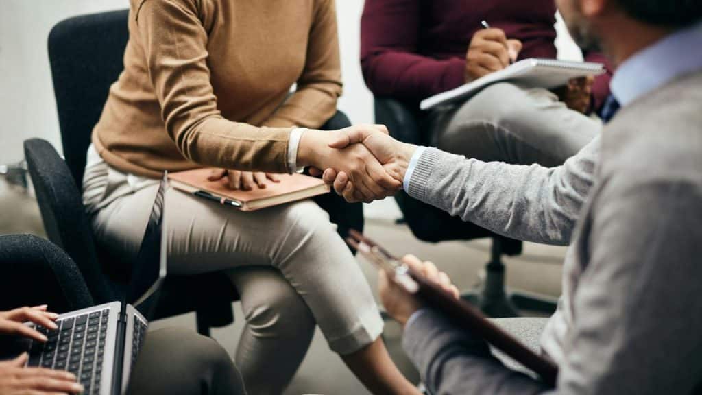 A group of people in a meeting with two individuals shaking hands.