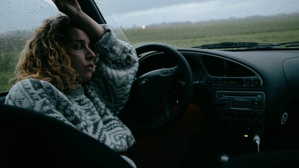 A woman sits in a car on a rainy day, looking out the window.