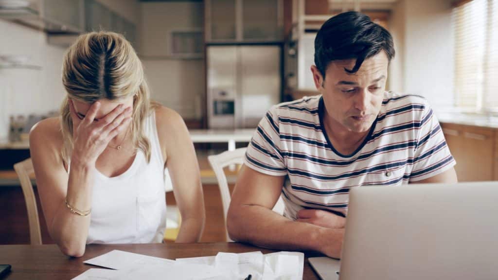 A woman covers her face beside a man in a striped shirt looking at a laptop.