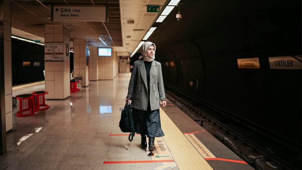 A woman holding a bag walking on a platform while looking to the side.