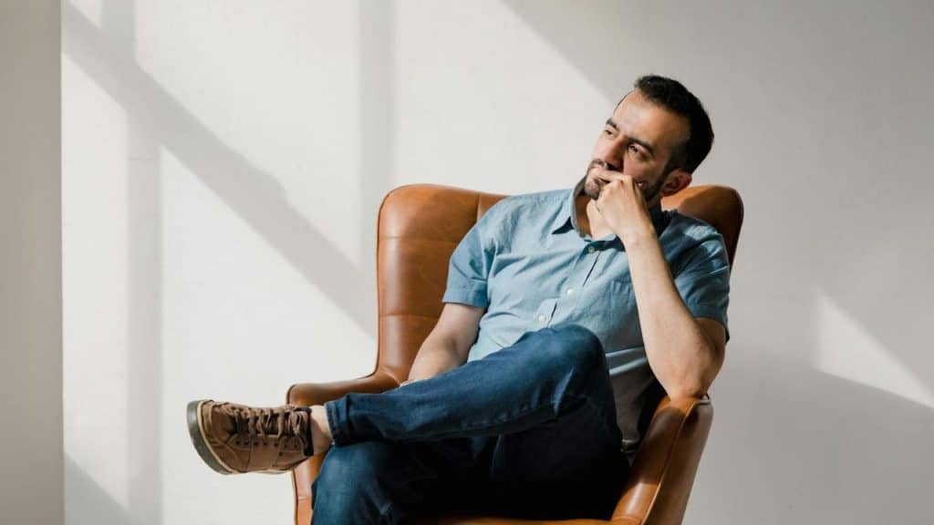 A man sits in a leather chair with his hand on his chin, looking away.