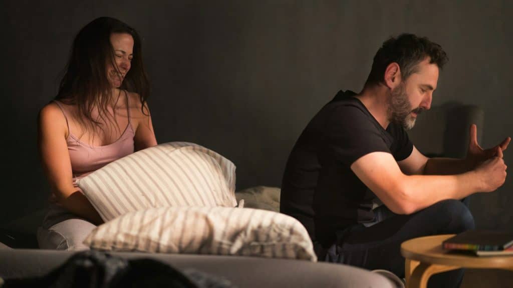 A man is sitting on a corner of a bed while a woman is crying while sitting next to her.