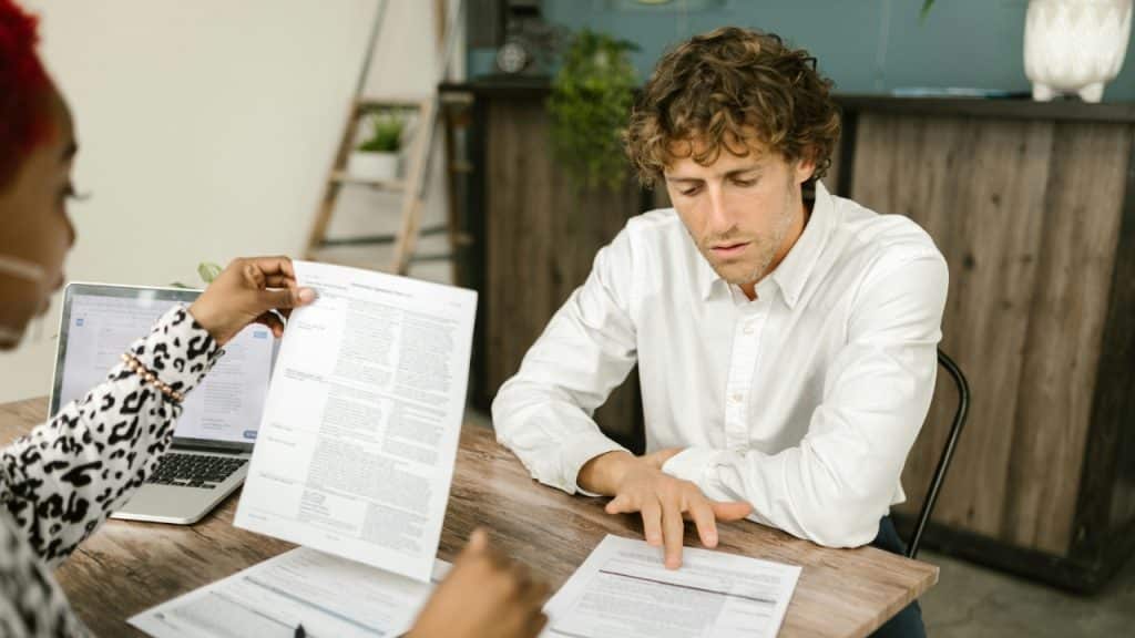 A person in a patterned shirt holds up a document for a man to see.