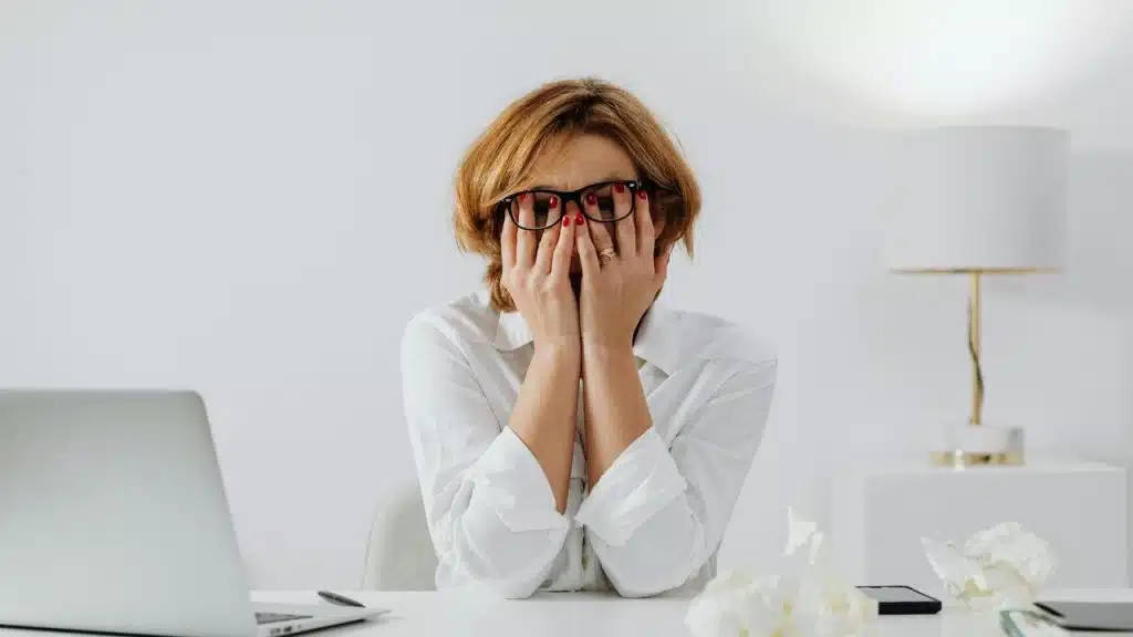 A stressed woman covering her face while sitting at a desk.