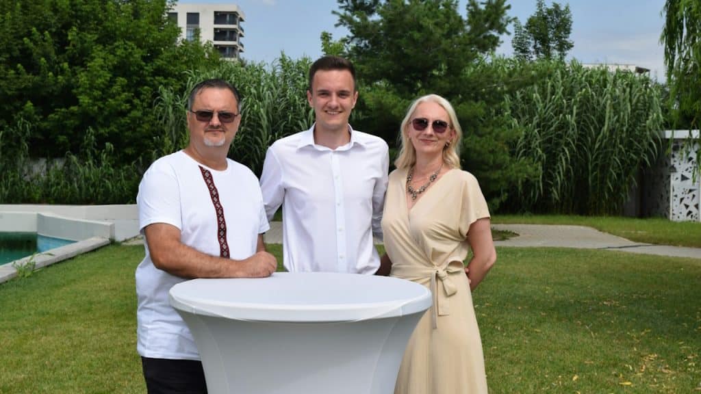 A young man is standing with his parents outdoors.