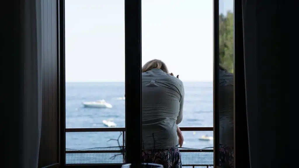 A woman leaning on a balcony railing looking out at the ocean.