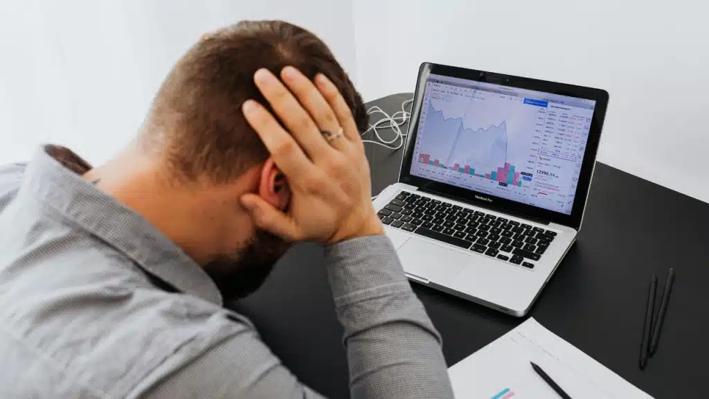 A man rests his head in his hands while looking at a laptop screen.