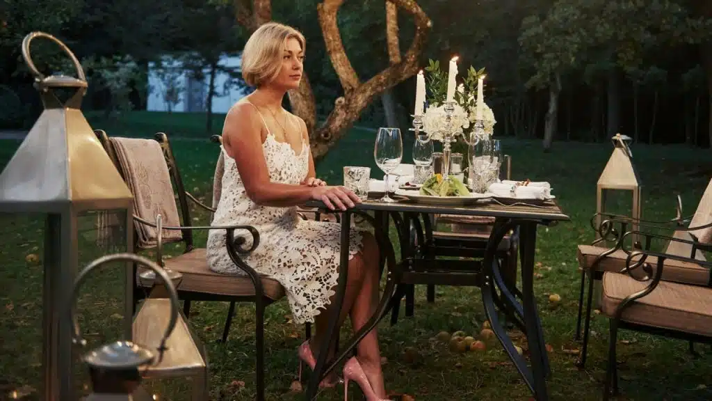 A woman in a white dress sits at an outdoor table set with candles and flowers.