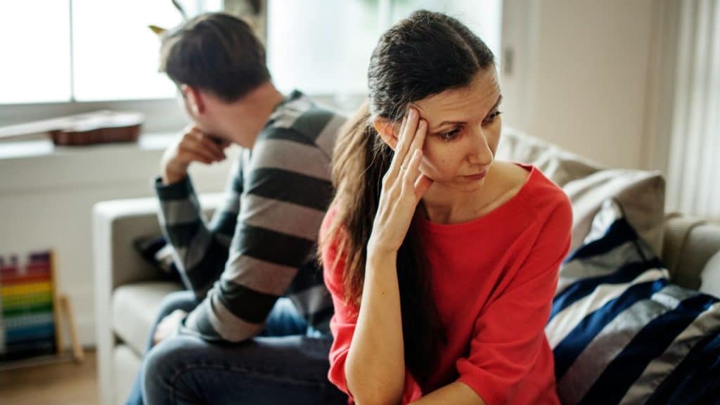 A woman in red rests her head on her hand while a man sits behind.