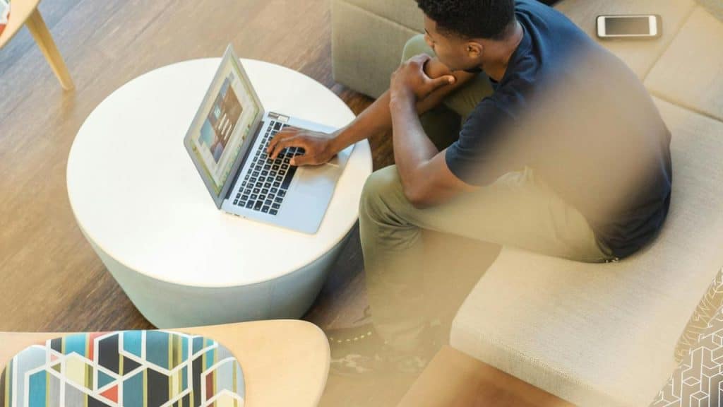 A man sitting on a couch and using a laptop at a coffee table.