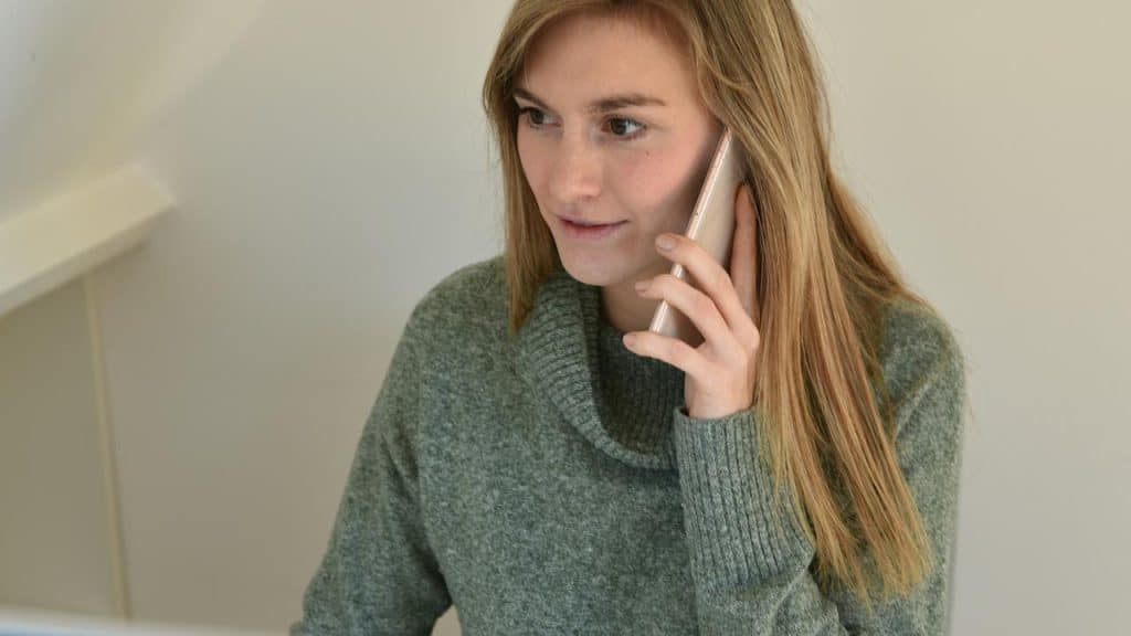 A woman in a sweater talks on a smartphone indoors.