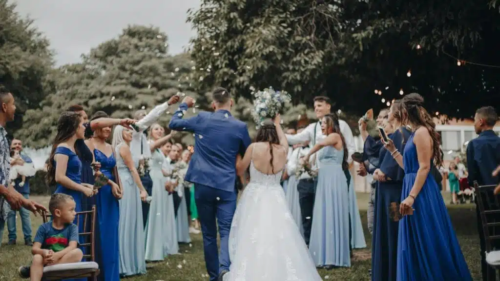 A bride and groom walk through cheering guests as confetti falls at an outdoor wedding.