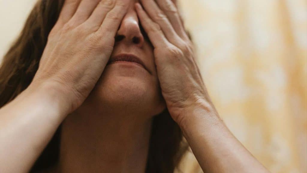 A woman covering her face with both hands in warm light.