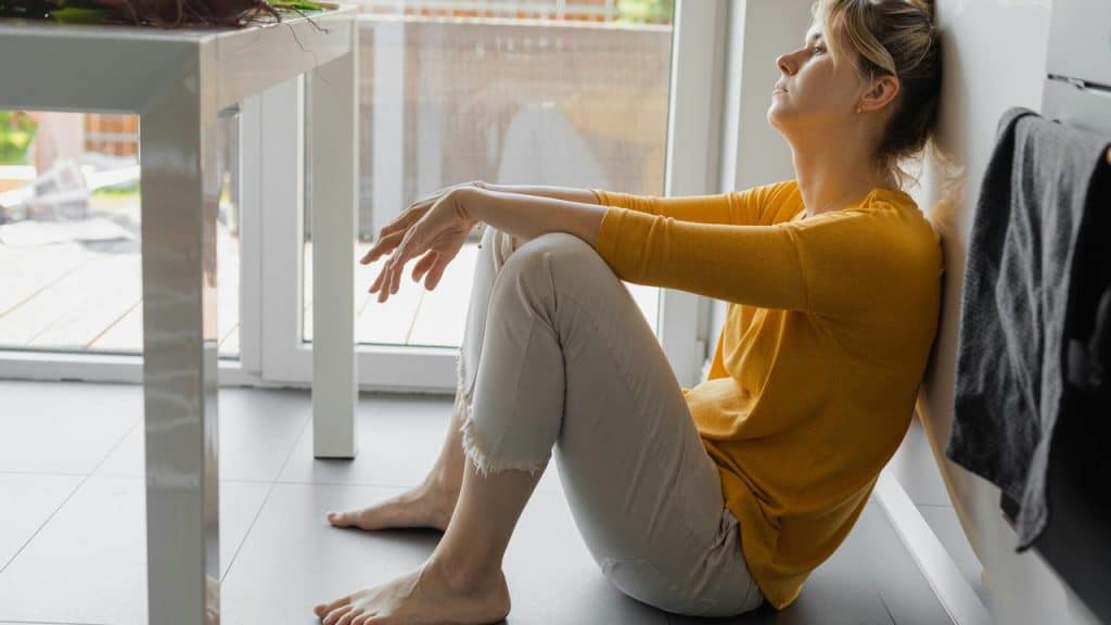 A woman sitting on the floor by a window, resting thoughtfully.