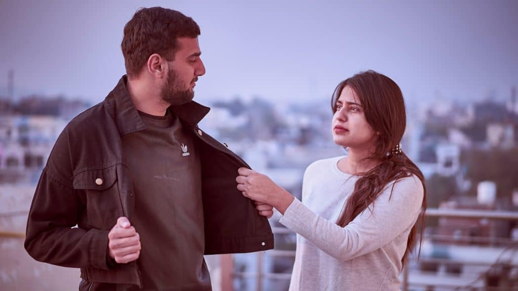 A woman grabbing the jacket of her boyfriend who is trying to move away.
