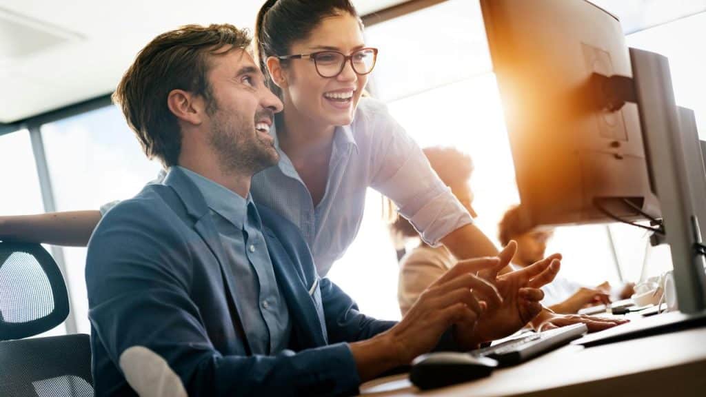 A man and woman smiling while working together at a computer in an office.