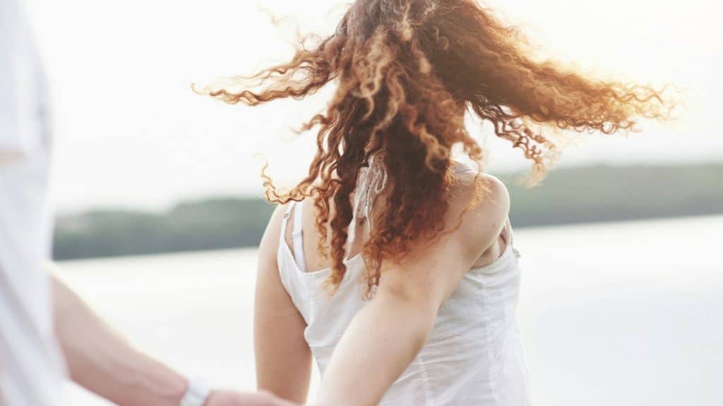 A woman with long curly hair spins around outdoors, her back facing the camera