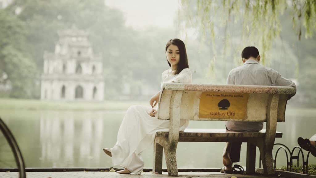 Man and woman sitting on a bench by a body of water.