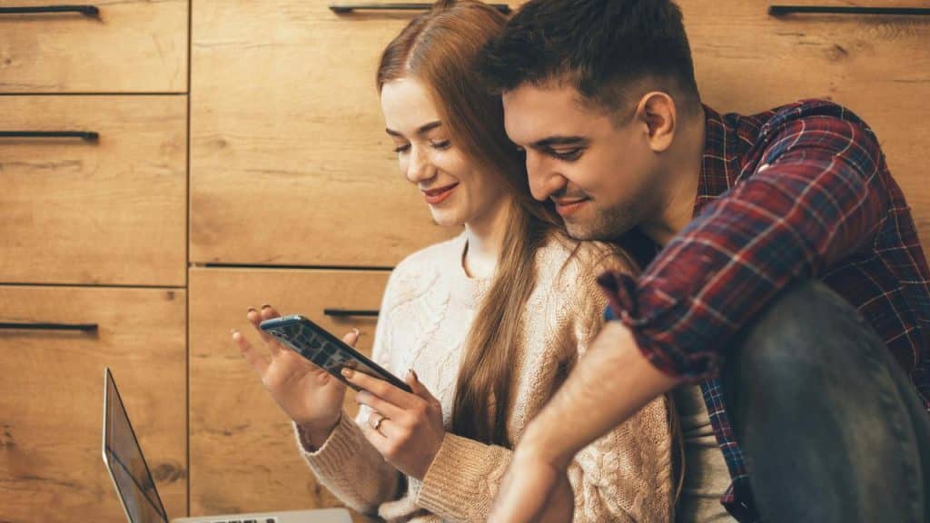 A couple sits together indoors while looking at a smartphone.