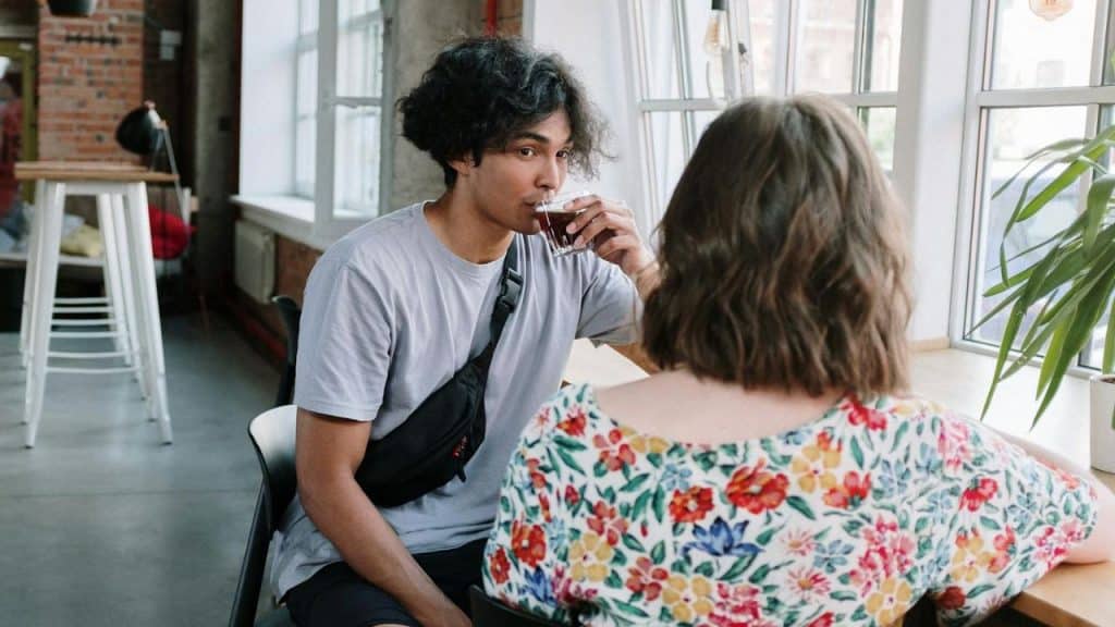 A man drinks from a glass while looking at a woman sitting across from him.