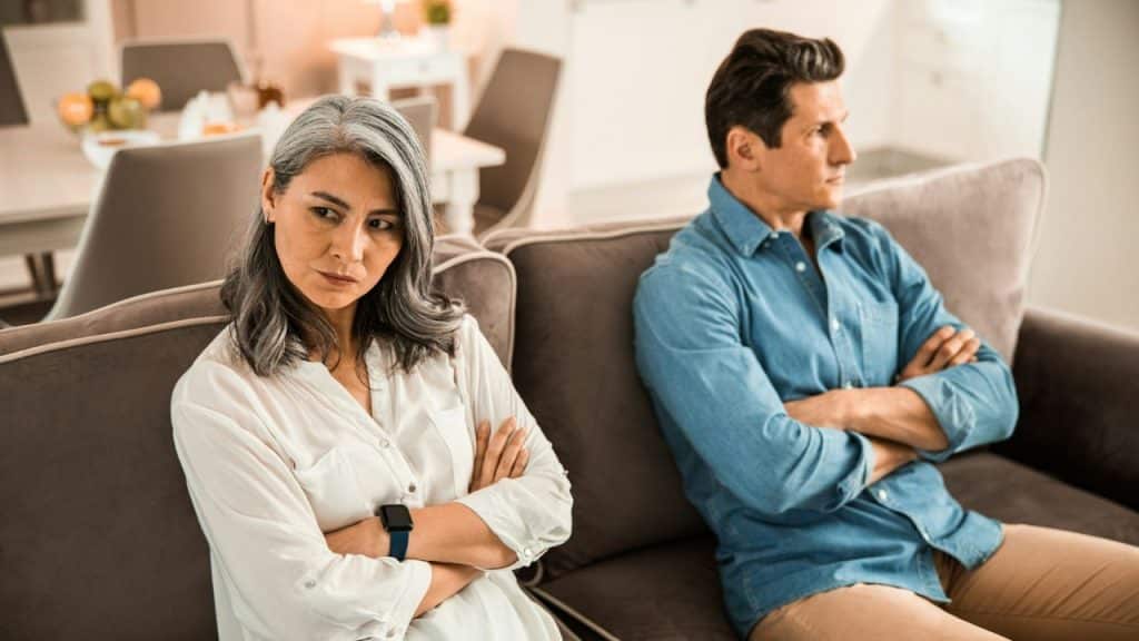 A man and a woman sit on a couch with arms crossed, looking away.