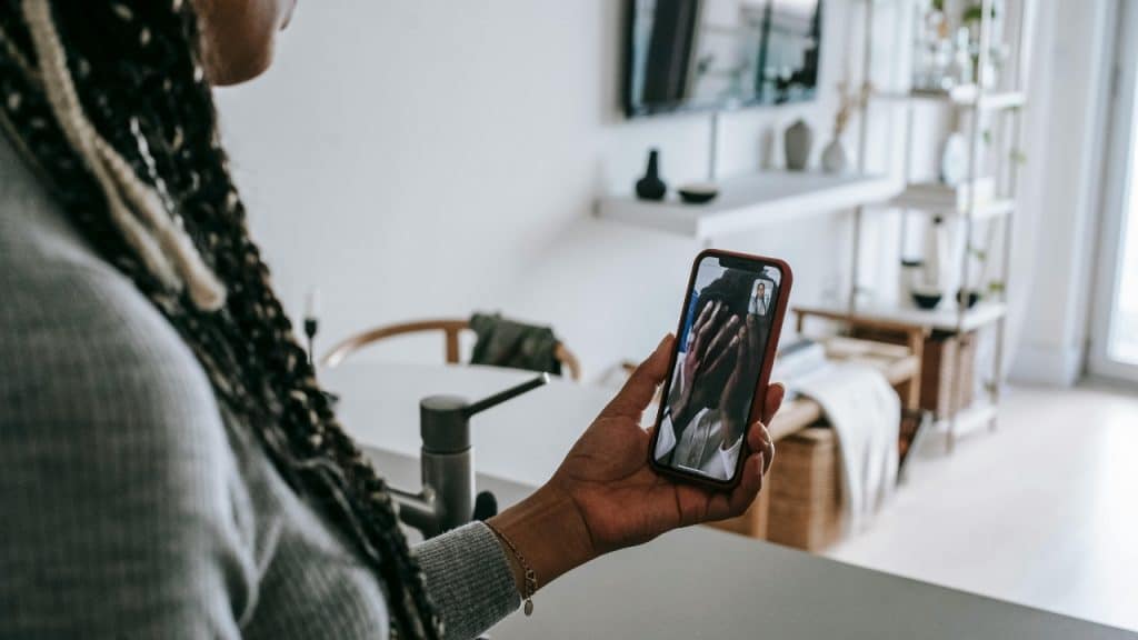 A person holds a smartphone displaying a video call of a man covering his face.