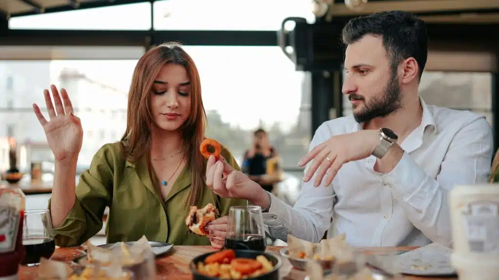 A man and woman sit at a restaurant table with food, looking away from each other.