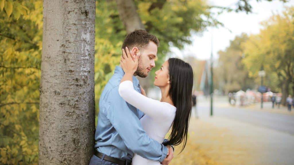 A couple standing close together by a tree, sharing an intimate moment.