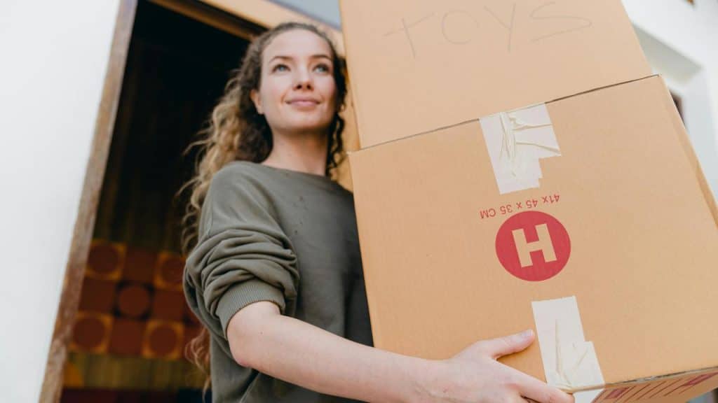 A woman carrying cardboard boxes while moving into a home.