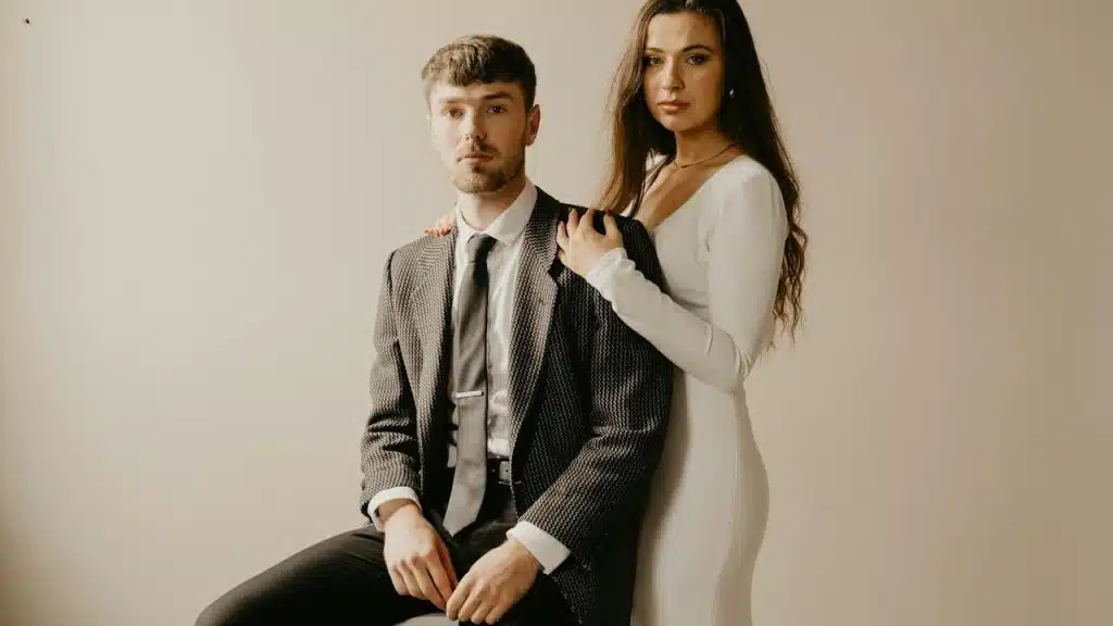 A woman resting her hands on a sitting man’s shoulders while she stands behind him.
