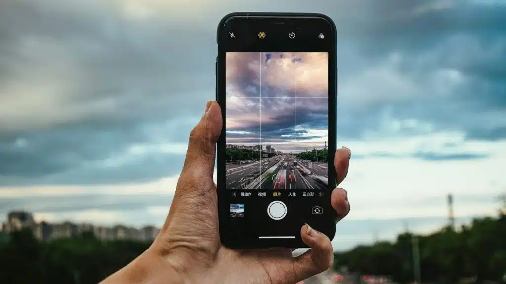 A hand holds a smartphone displaying a camera view of a highway under a cloudy sky.