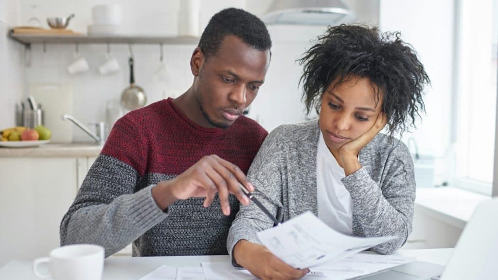 A frustrated couple checking monthly bills while sitting at a table together.