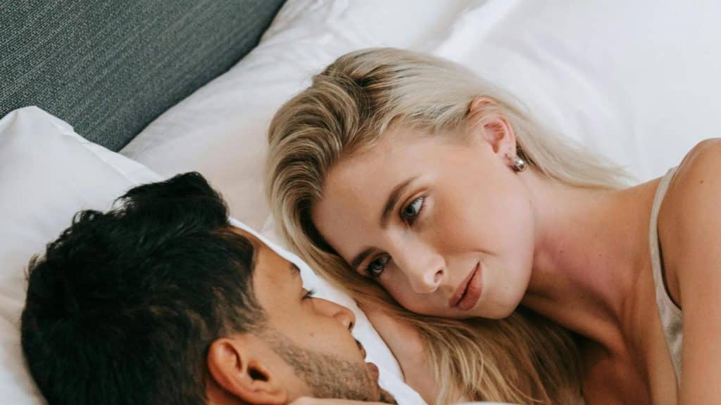 A couple lies in bed facing each other in a quiet moment.