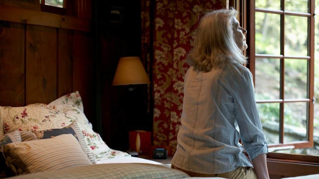 A woman sitting on the bed in front of a window in the morning.