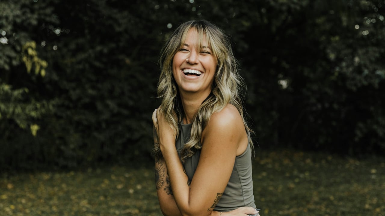 A woman laughing while holding her arms around her as she stands outdoors.