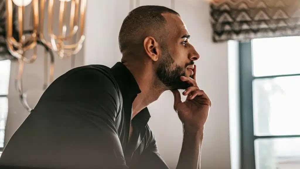 Profile view of a man with a beard and buzz cut, resting his chin on his hand.