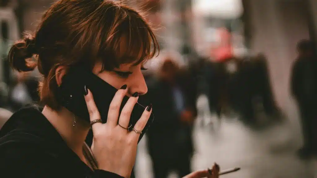 A woman talking on a phone while holding a cigarette on a busy street.