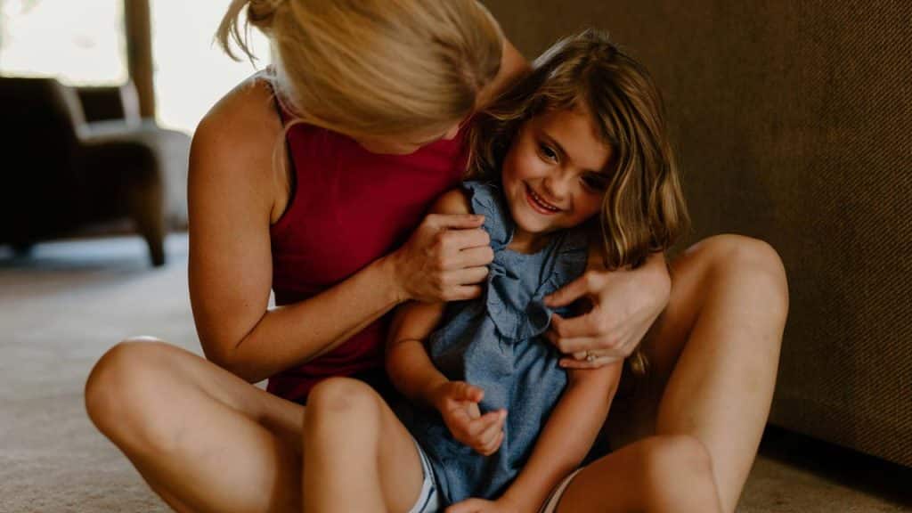 A woman sitting on the floor hugging a smiling young child.