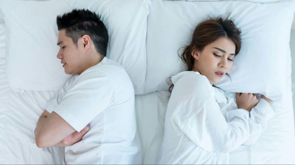 A man and woman lying in bed but facing away from each other