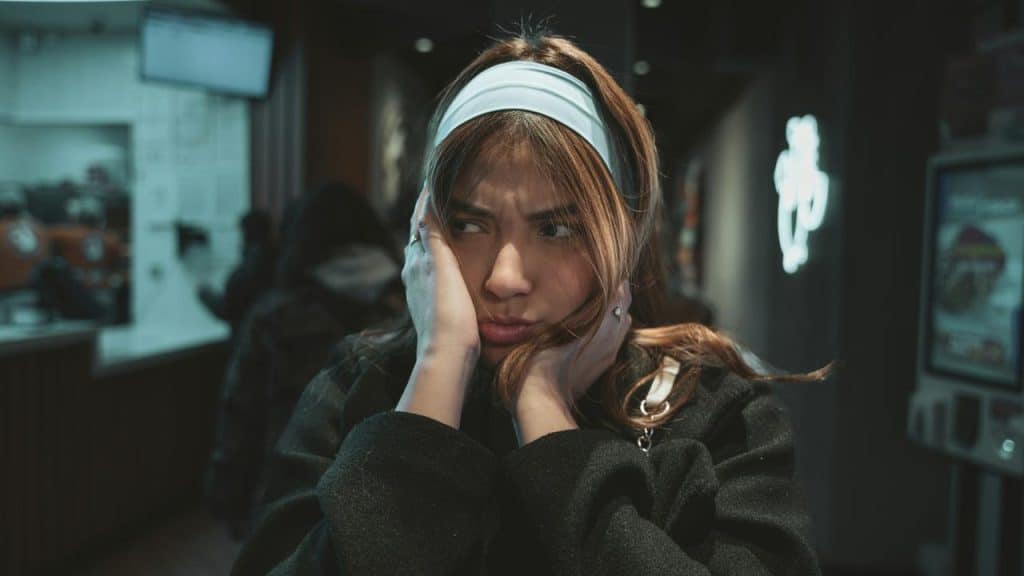 A person indoors holds their hands over their ears with a frustrated expression.