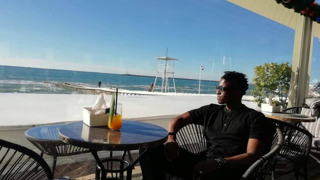A man sitting at a seaside café table looking out at the ocean.