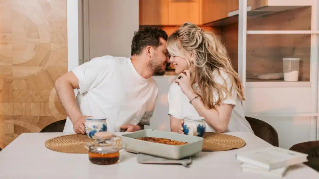 A man and woman lean toward each other over a table with food and mugs.