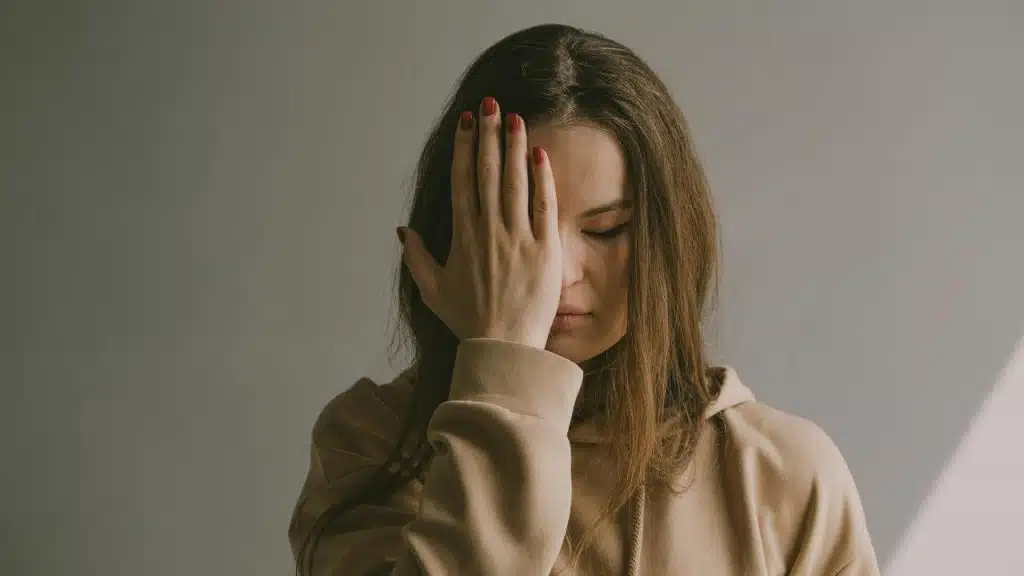 A woman covering one eye with her hand against a plain background.