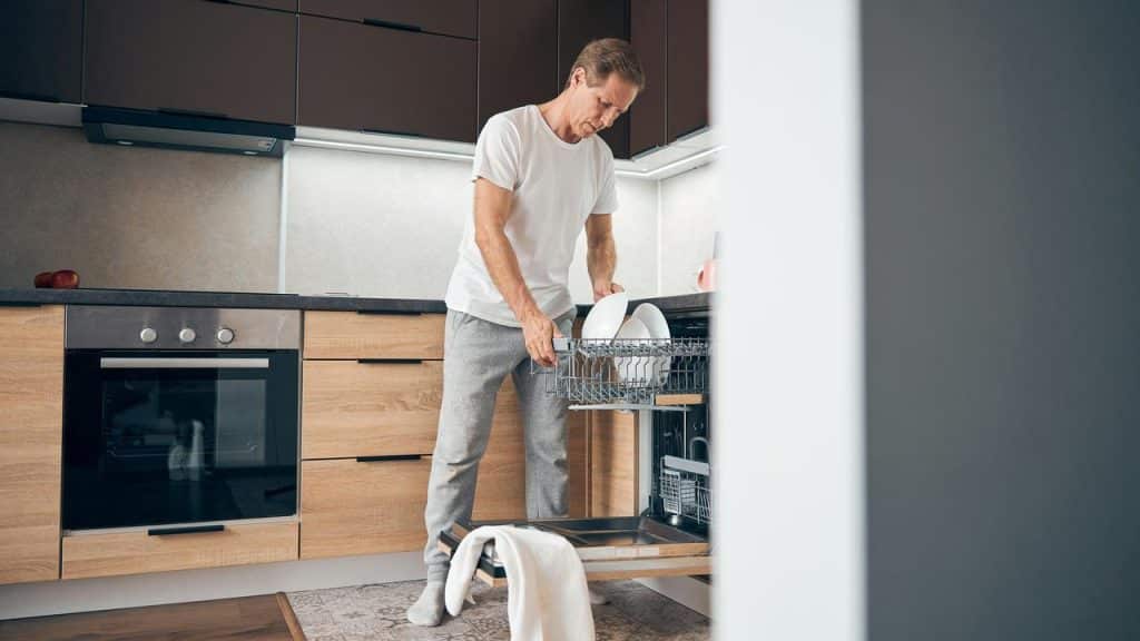 A man unloading dishes from a dishwasher in a modern kitchen.