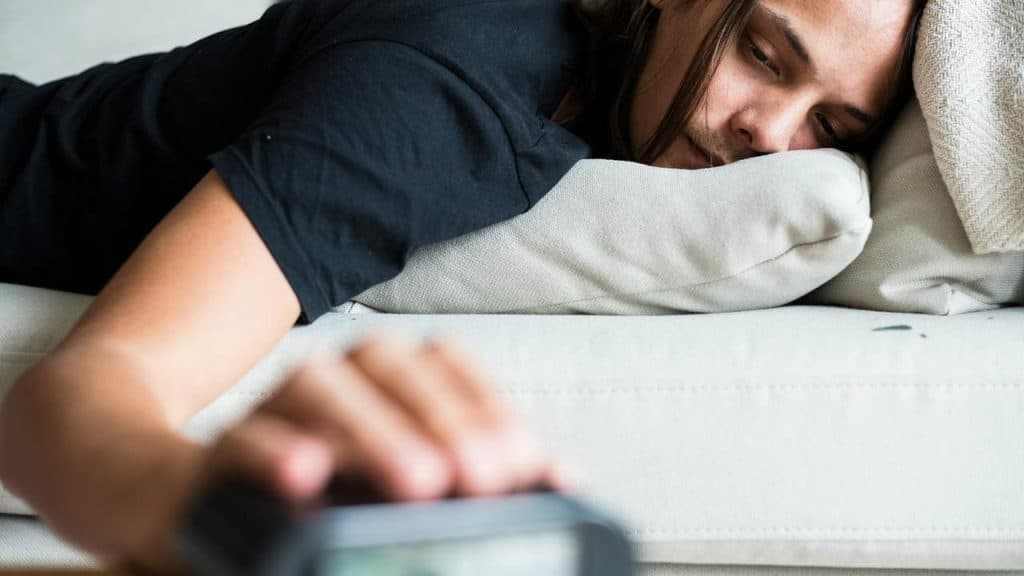 A person lying on a couch and reaching for a smartphone.