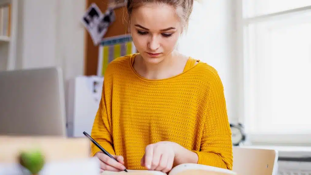 A young woman studying and writing in a notebook at a desk.